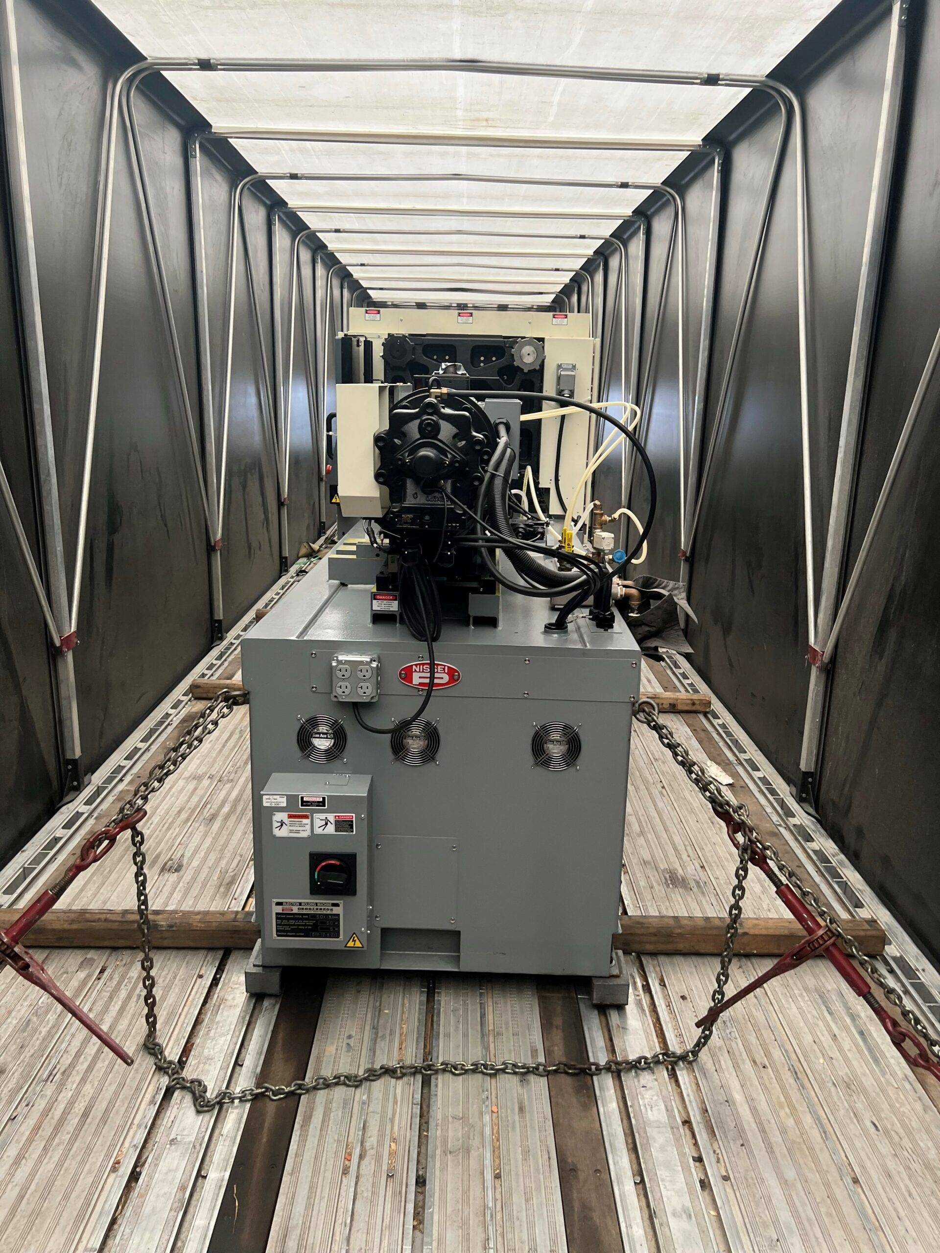 Step deck conestoga trailer being loaded with a large injection molding machine using a forklift.