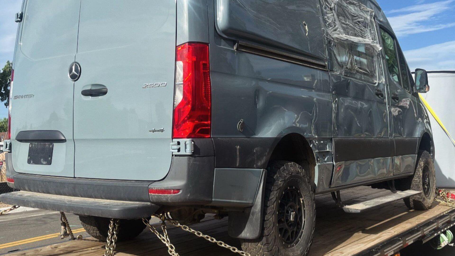 Damaged Mercedes Sprinter 2500 van secured on a step deck trailer for transport
