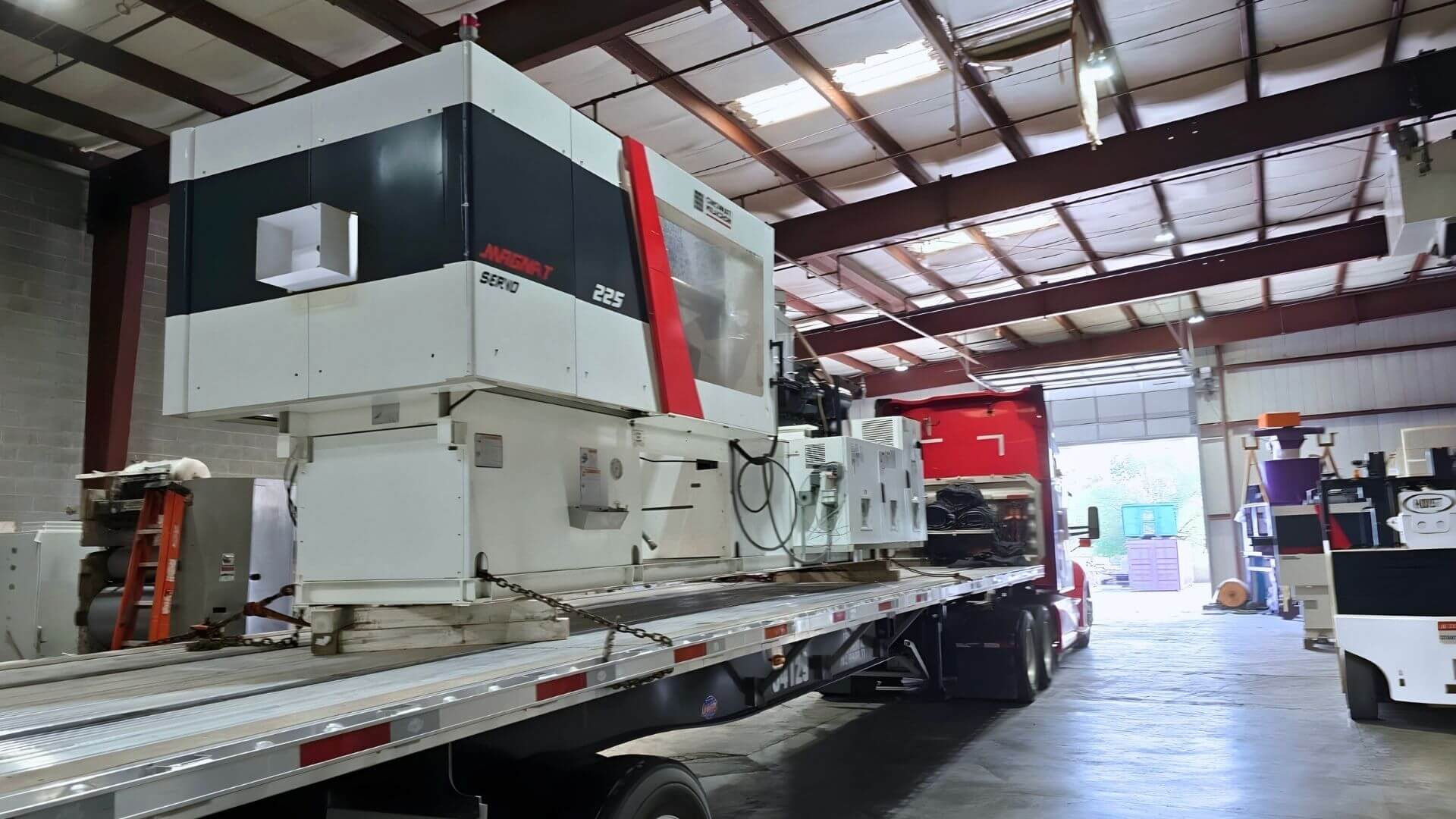 Large 225-ton Cincinnati injection molding machine loaded and secured on a flatbed trailer for transport by Abound Transport.