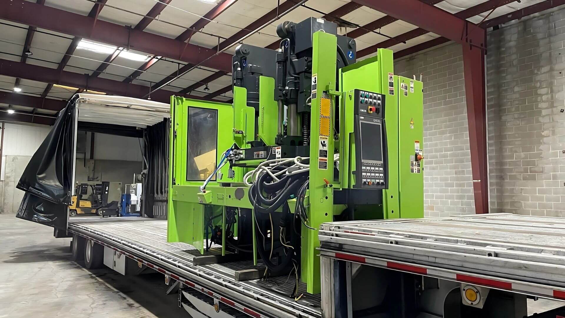 Green injection molding machine secured on a flatbed trailer for transport by Abound Transport.
