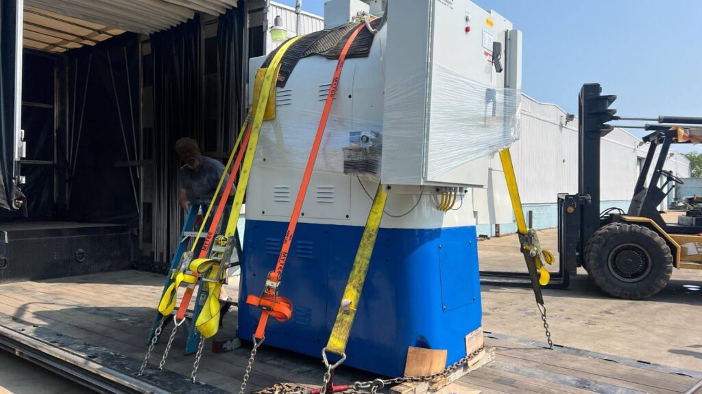 Grinding machine secured on a double drop Conestoga trailer for machinery transport by Abound Transport.