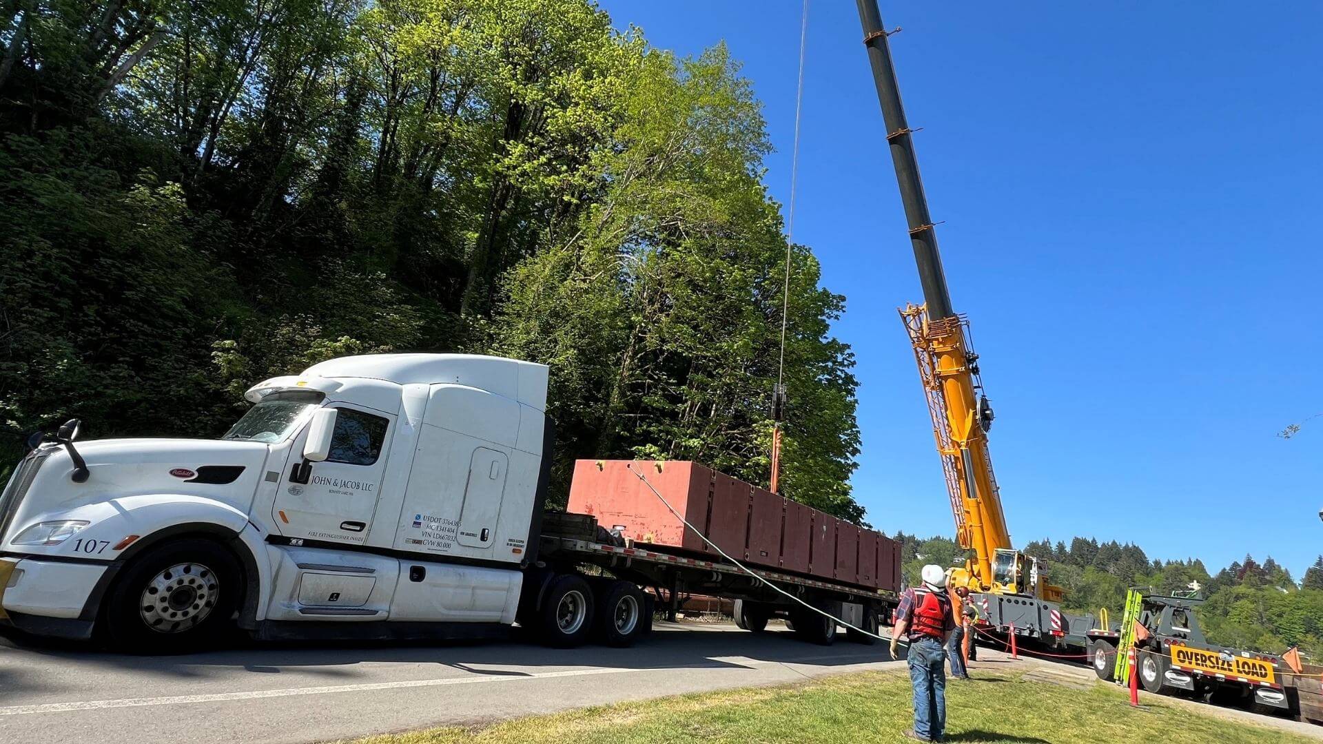 Jobsite and Conestoga delivery of a flatbed shipment flexi-float being crane unloaded showing Abound Transport Level of expertise in being on time crane appointment
