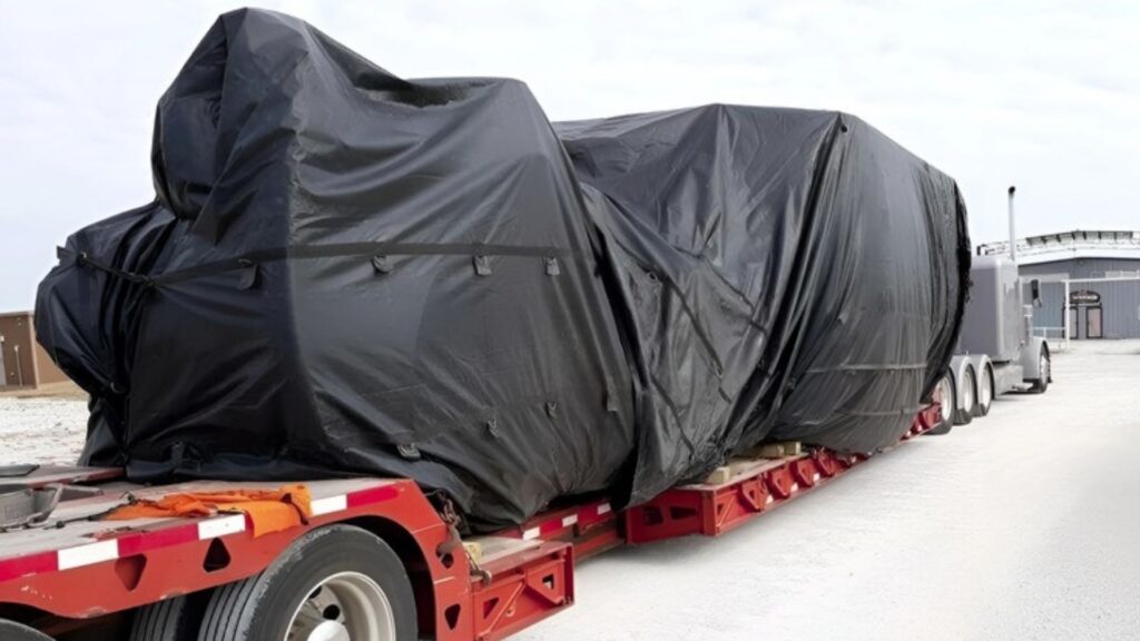 Tarped oversized machinery load secured on a flatbed trailer for long-haul transport