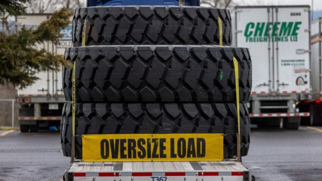 Oversize load banner on flatbed trailer hauling heavy machinery tires
