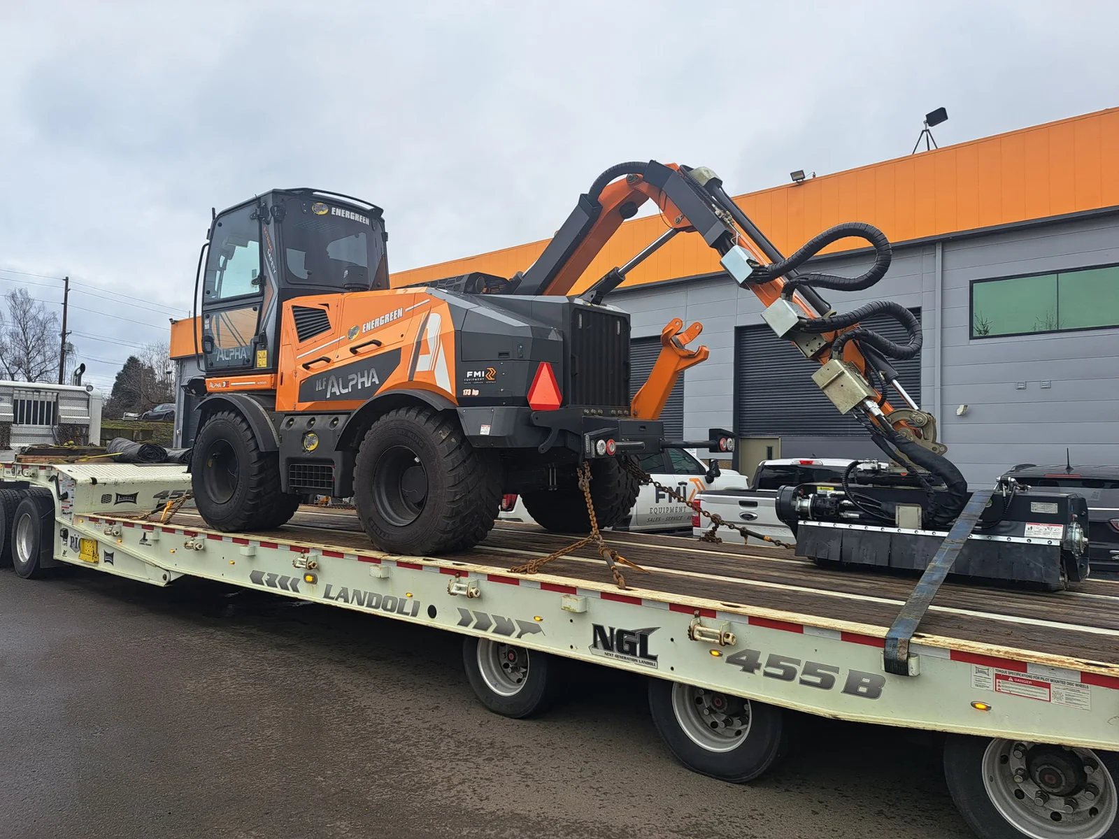 Compact wheeled excavator secured onto a flatbed step deck trailer for heavy machinery transport