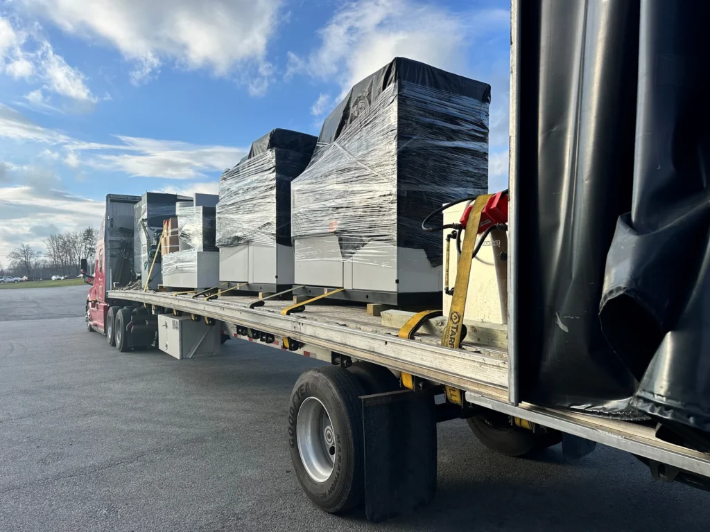 Conestoga flatbed trailer hauling shrink-wrapped industrial machinery secured with heavy-duty cargo straps