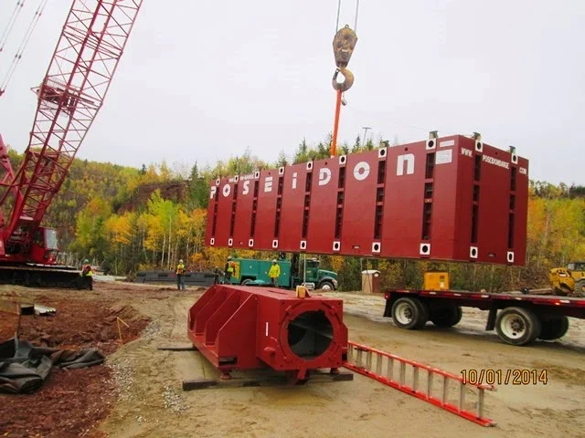Heavy-duty lattice boom crawler crane lifting a large red Poseidon barge section onto a flatbed trailer