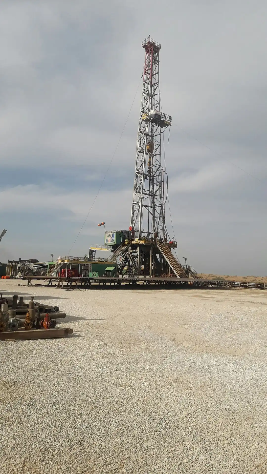 Tall onshore oil drilling rig tower on a gravel worksite representing oilfield equipment hauling and energy freight logistics
