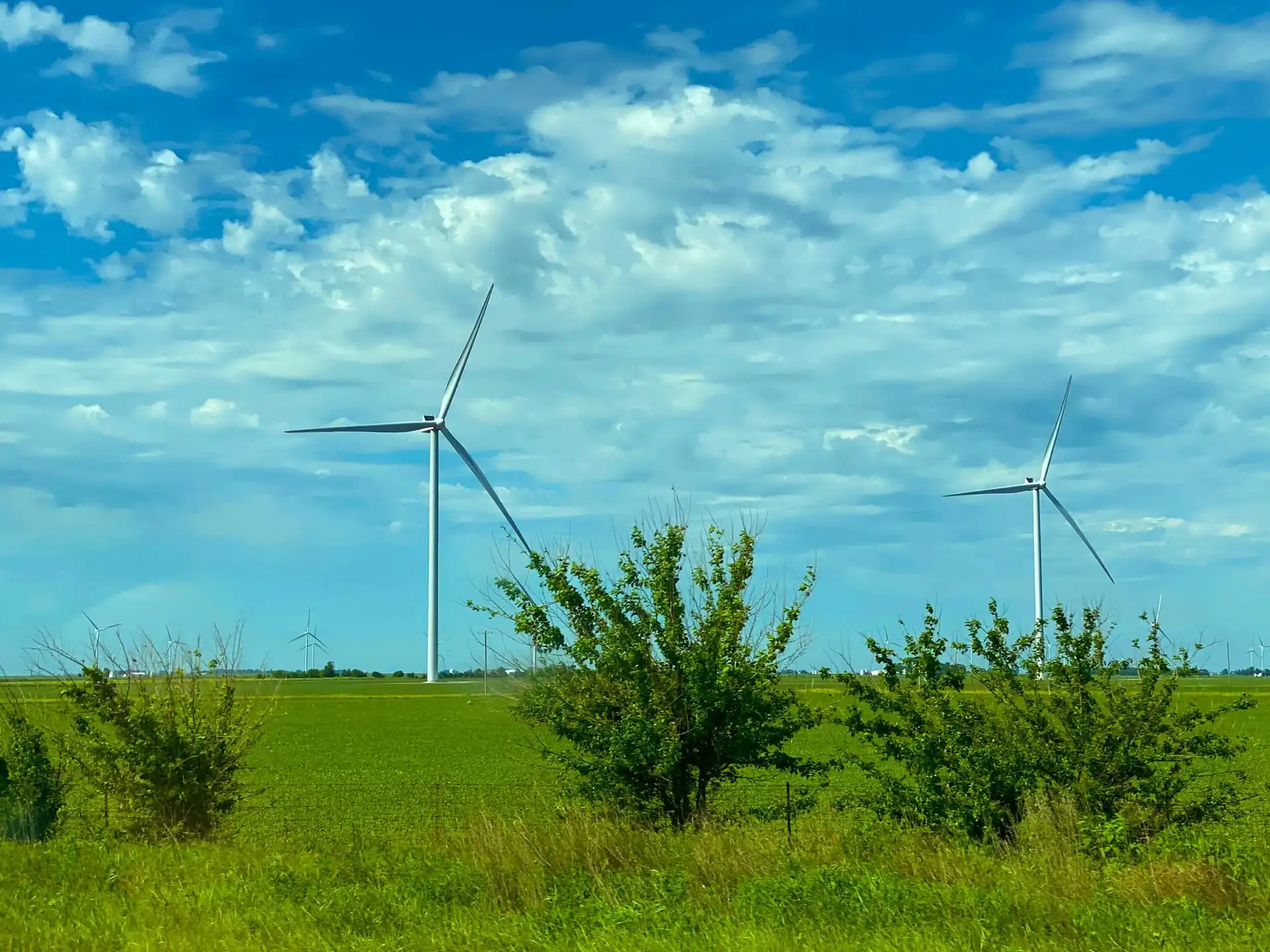 Wind turbine farm in a vibrant green rural field under a blue cloudy sky for renewable energy heavy haul freight logistics