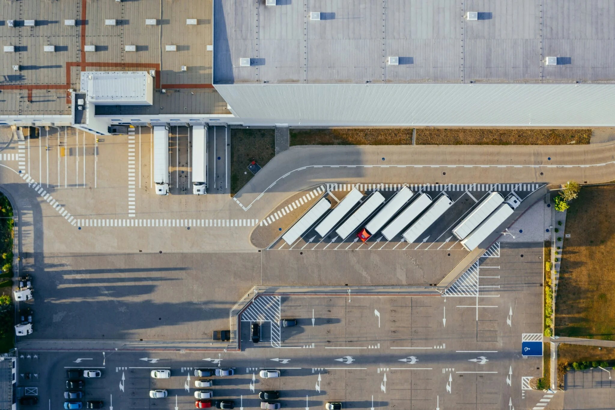 Aerial top-down view of a modern logistics distribution center and warehouse with semi-trucks parked at loading docks