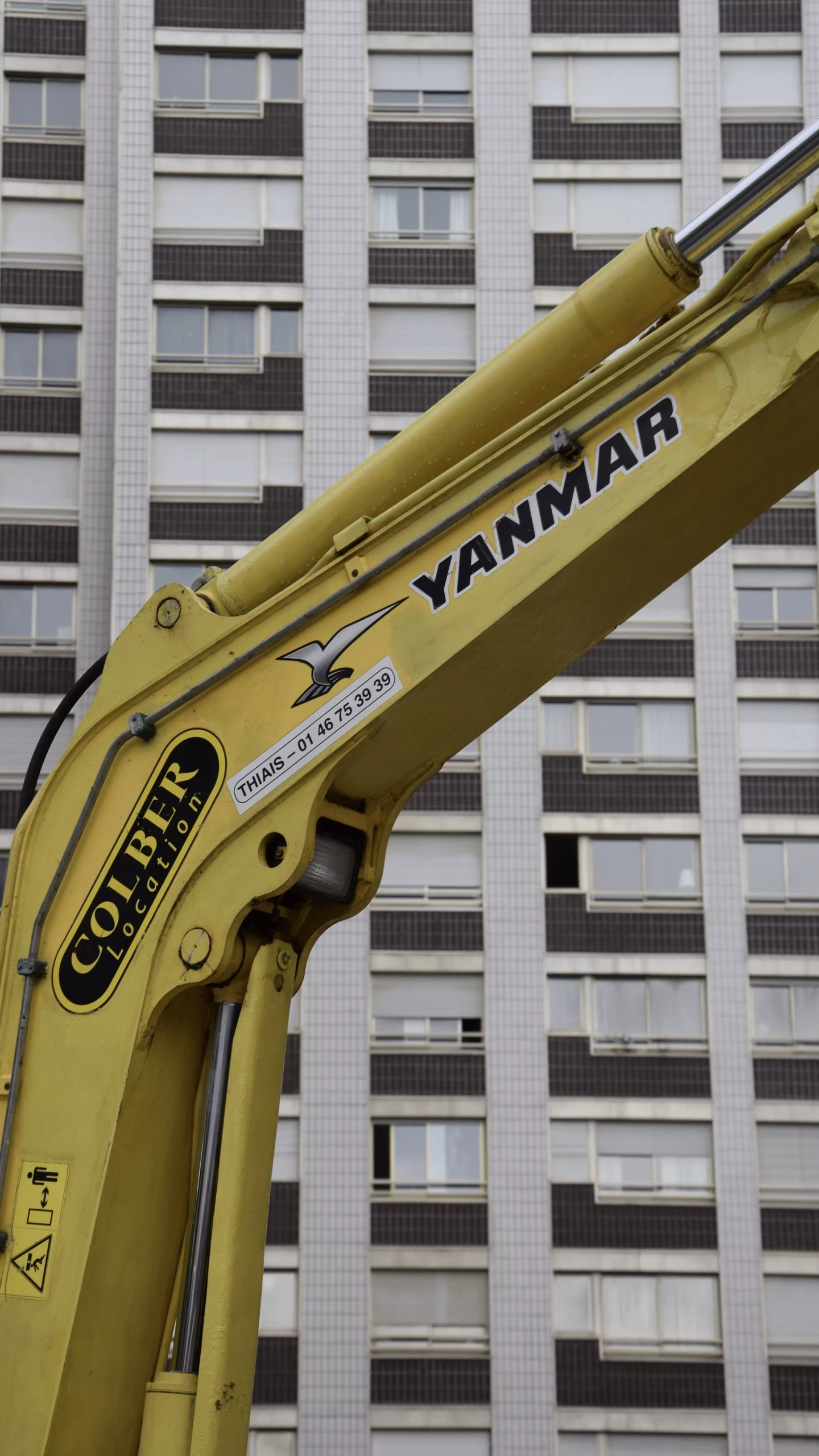Yellow Yanmar excavator boom and hydraulic arm at an urban construction building site