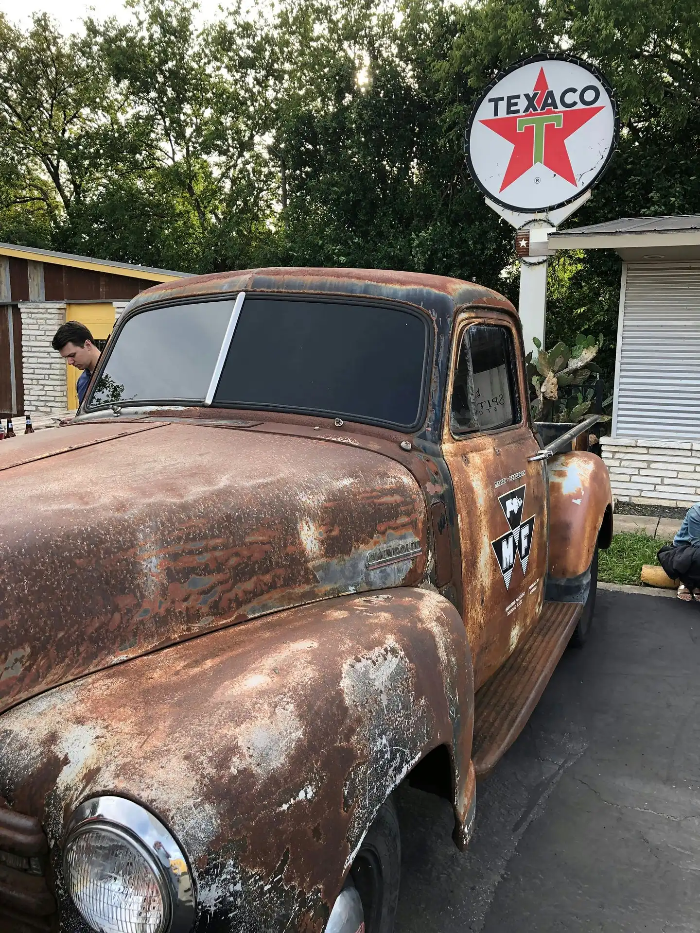 Antique rusty Chevrolet pickup truck parked outside a vintage Texaco service station representing trucking industry heritage