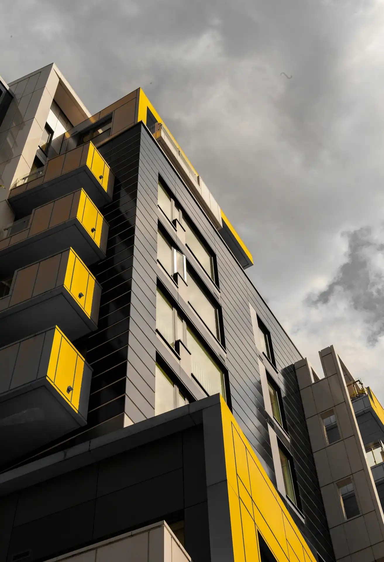 Modern residential building exterior featuring black facade panels and bright yellow balconies representing construction materials freight transport