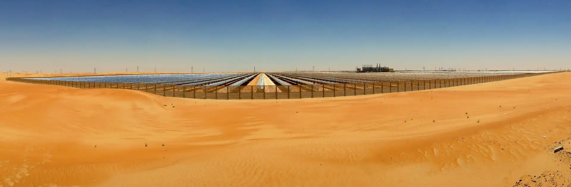 Massive concentrated solar power farm installation surrounded by orange desert sand dunes for renewable energy infrastructure logistics