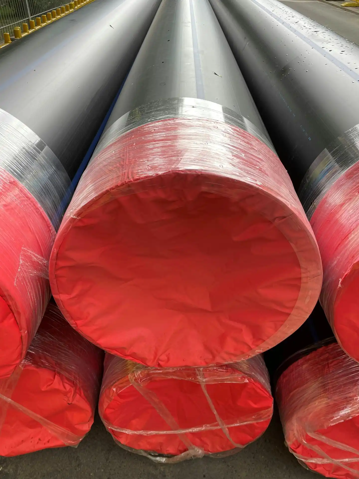 Stacked large diameter black industrial pipes with bright red protective end caps prepared for flatbed freight transport