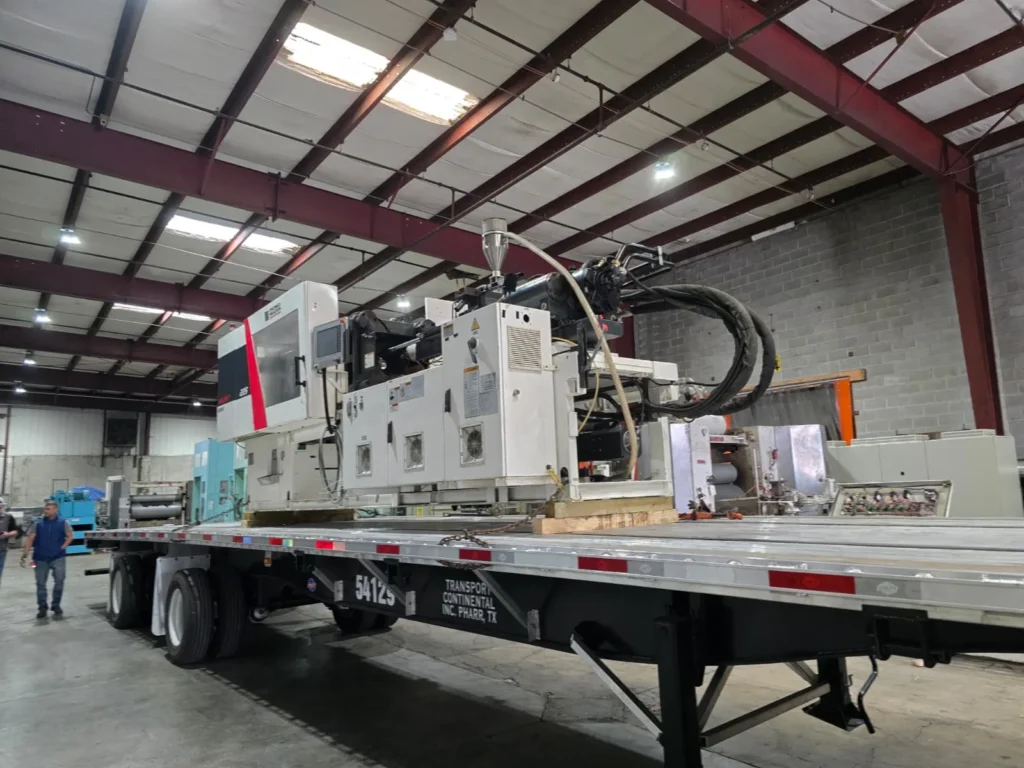 Industrial injection molding machinery secured on a flatbed semi-trailer inside a warehouse facility