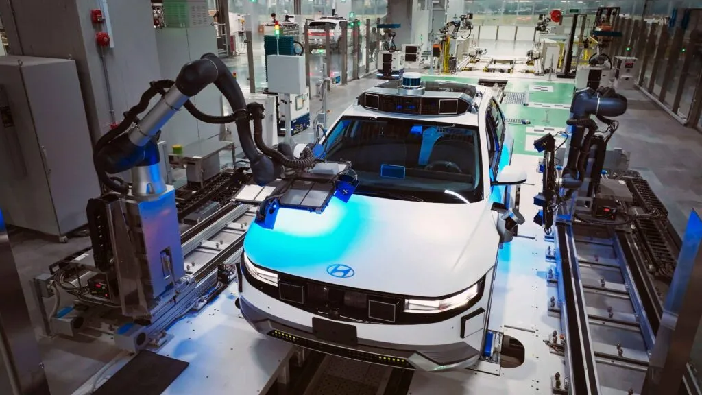 Robotic arms calibrating and inspecting an autonomous Hyundai electric vehicle on an automated factory production line