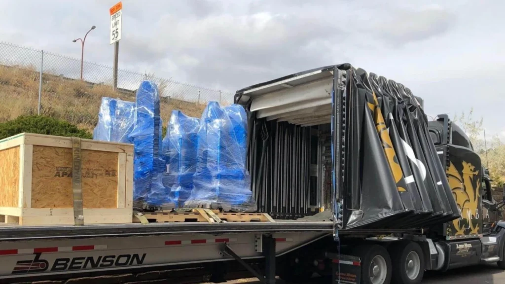Conestoga curtainside trailer loaded with crated freight and blue barrels for PTL shipping Abound Transport