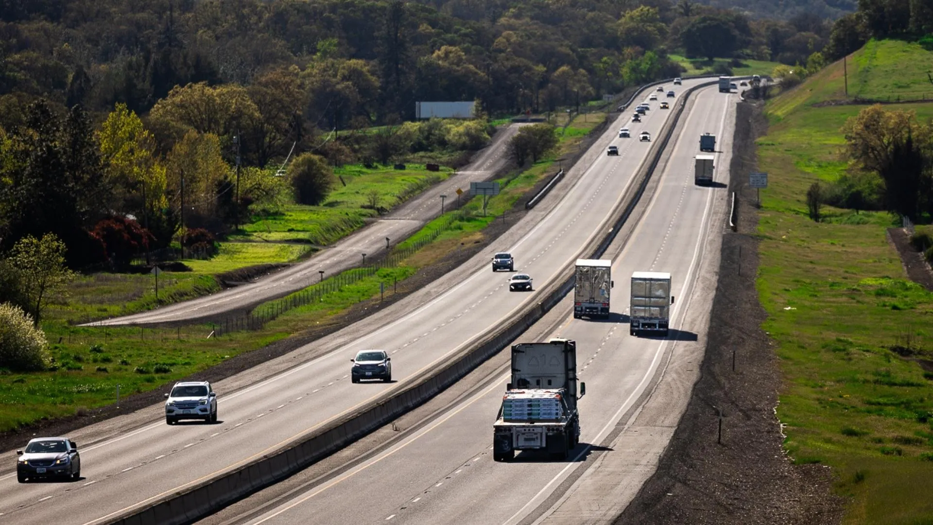 Semi-trucks and freight carriers hauling cargo along a multi-lane interstate highway corridor