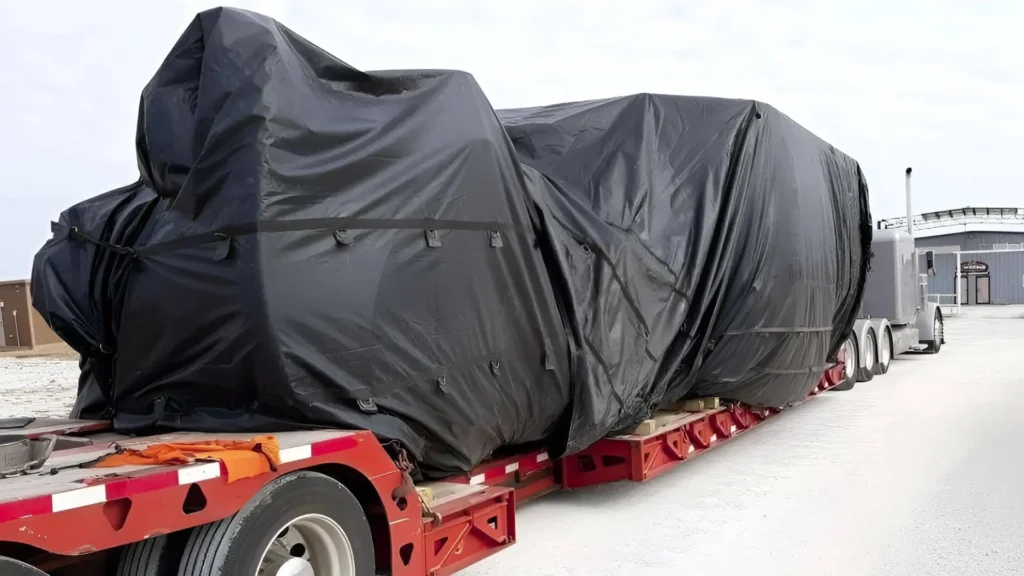 Heavy haul oversized machinery secured and tarped on a long-haul open-deck trailer for transport.