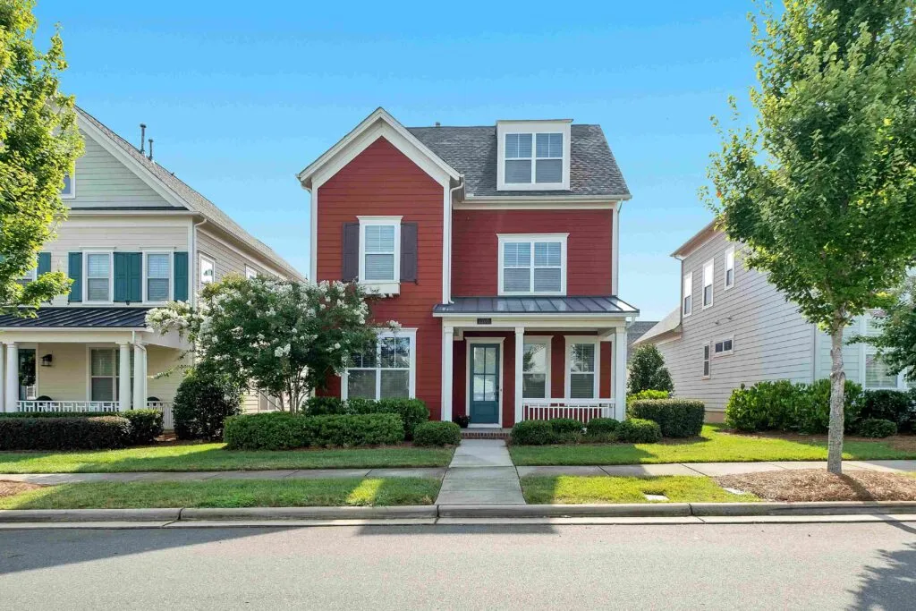 Charming two-story red suburban family home with white trim, front porch, and manicured green lawn