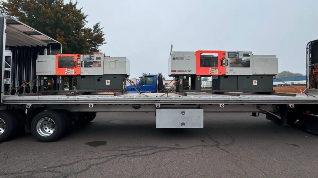 Red injection molding machines loaded and secured on a Conestoga flatbed trailer for transport by Abound Transport.