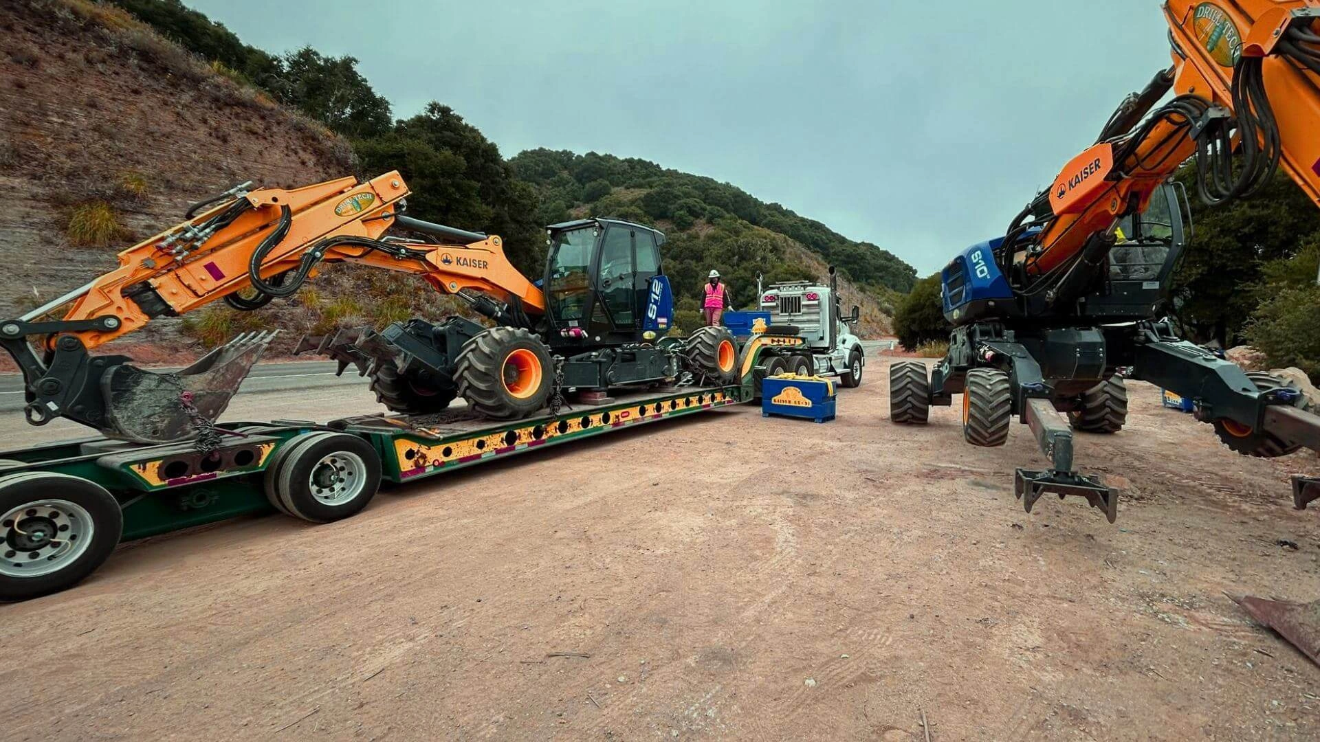 Specialized lowboy trailer hauling heavy Kaiser walking excavator machinery at a mountain job site