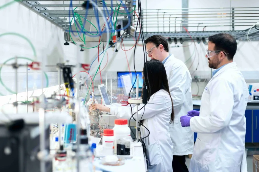 Team of scientists in white lab coats and safety glasses conducting chemical experiments in a modern research laboratory
