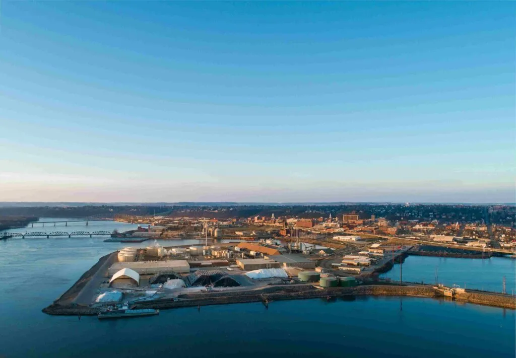 Aerial view of an industrial river terminal and storage facility located along a wide river near an urban town
