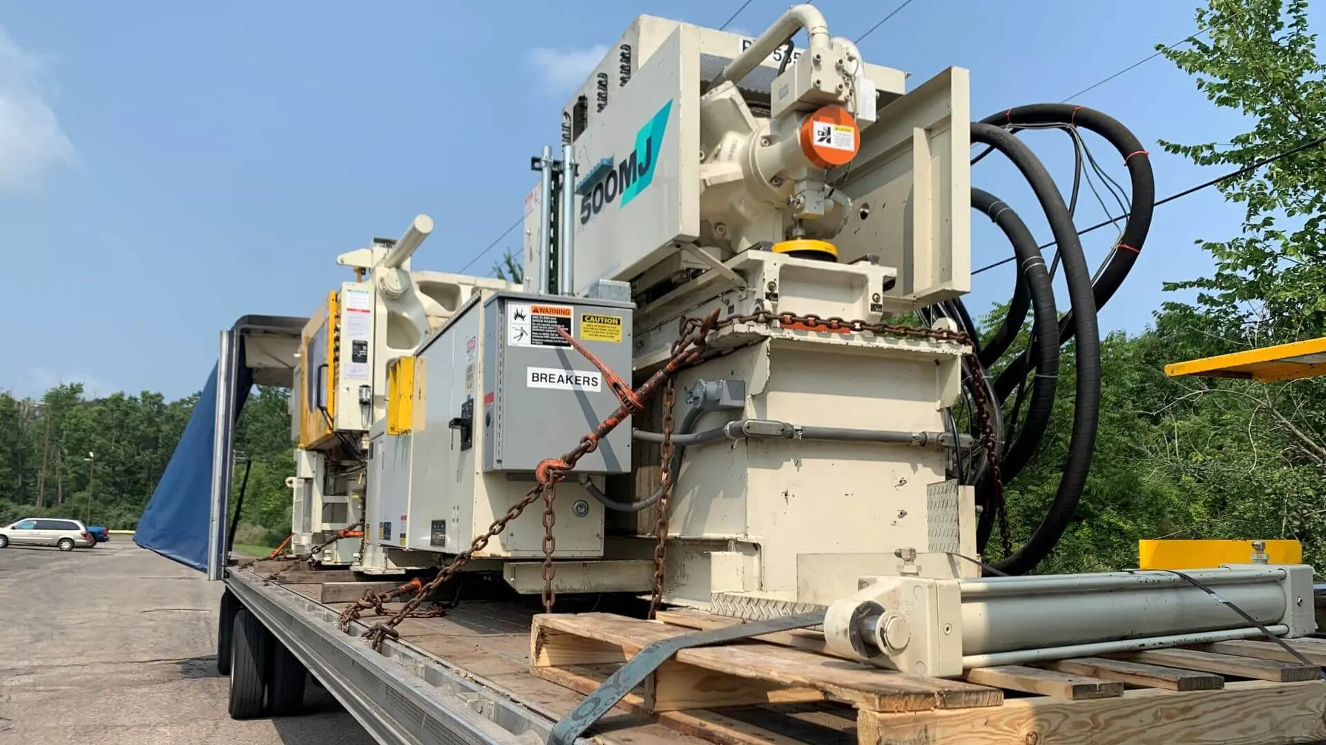 Mitsubishi 500MJ heavy industrial injection molding machine and hydraulic components chained to a flatbed trailer for machinery transport