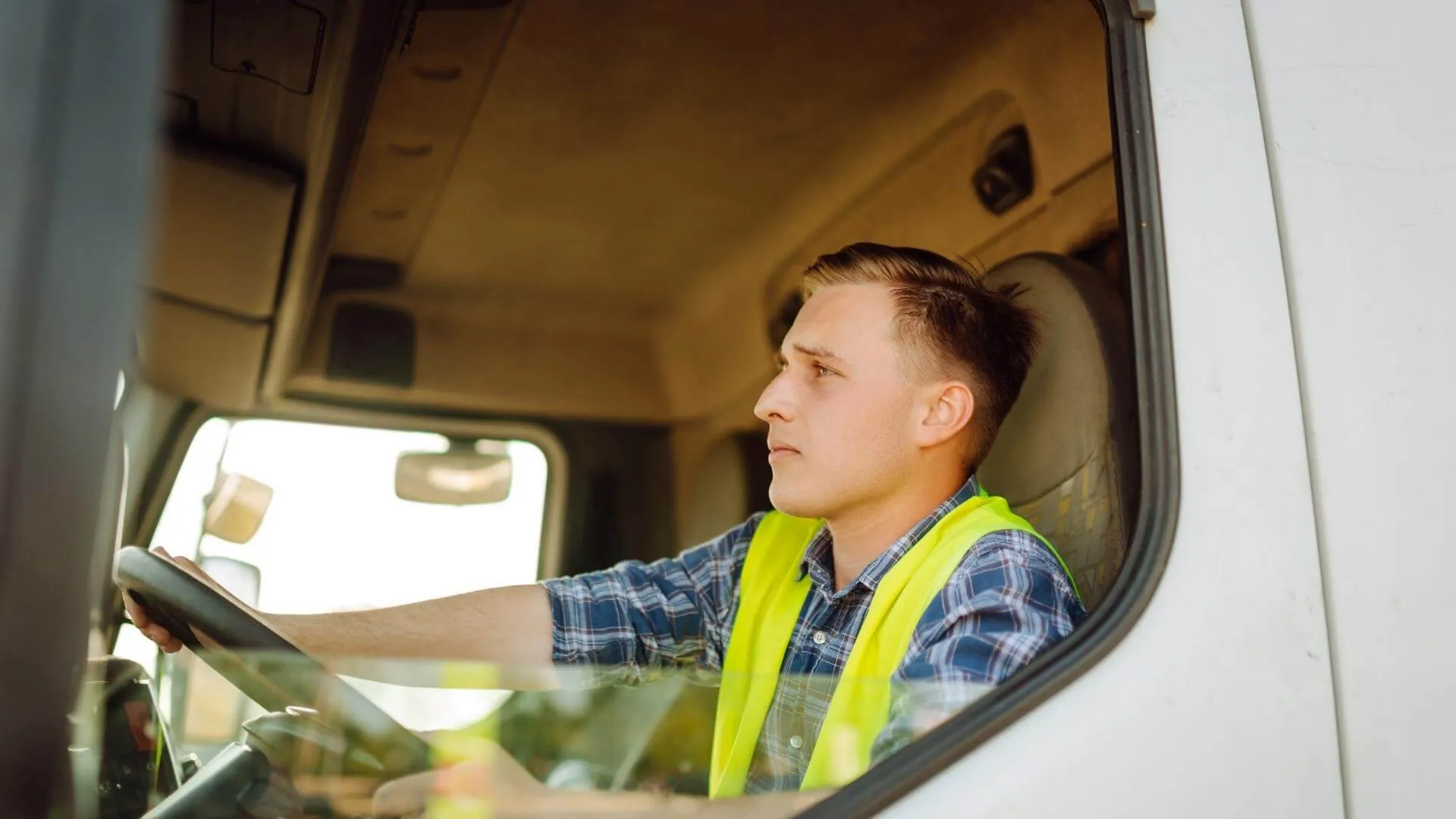 Professional truck driver in safety vest operating a commercial semi-truck cabin