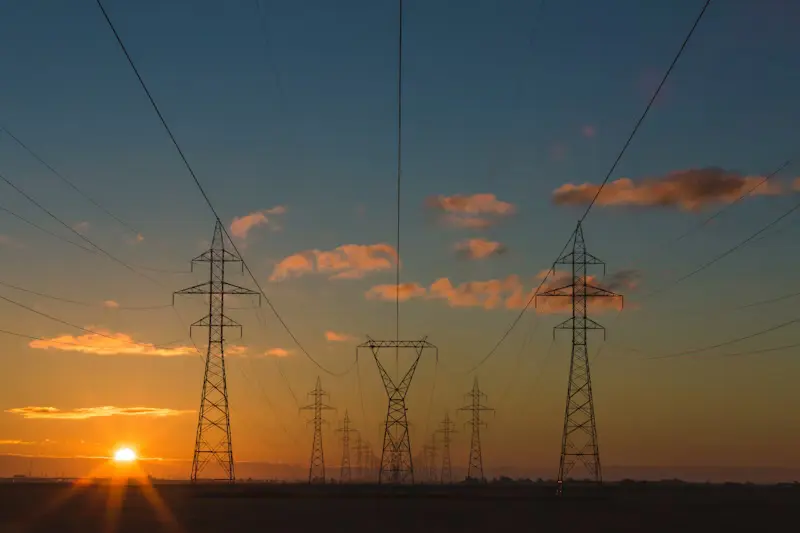 High-voltage power transmission lines and electrical grid towers silhouette at sunset