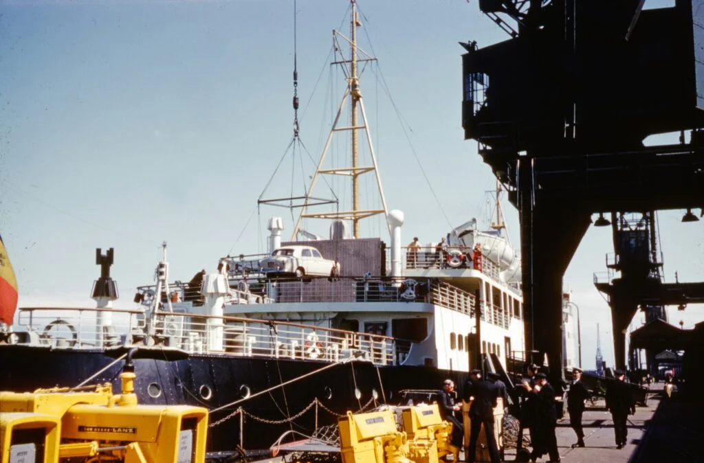 Vintage harbor crane hoisting a classic white car onto the deck of a passenger cargo ship at the docks