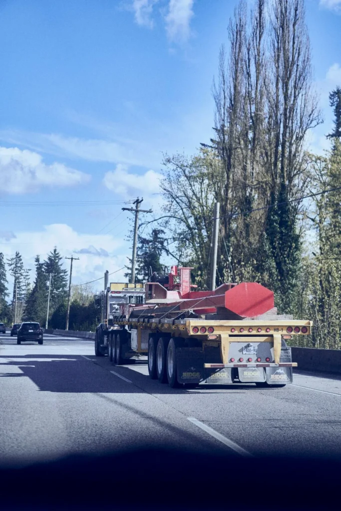 Rear view of a heavy-duty multi-axle flatbed semi-truck transporting long red structural steel beams on a highway