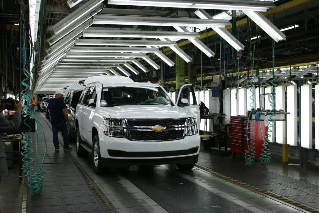 White Chevrolet SUV on an automotive factory assembly line under bright overhead inspection lights