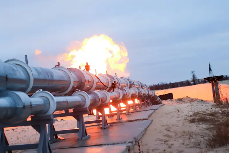 Industrial gas pipeline infrastructure with active natural gas flare in remote oilfield