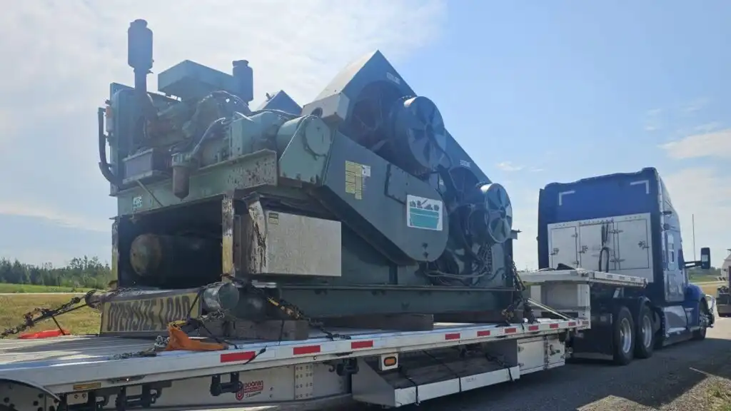 Oversize load RGN lowboy semi-trailer transporting heavy industrial stamping press machinery secured with heavy-duty transport chains