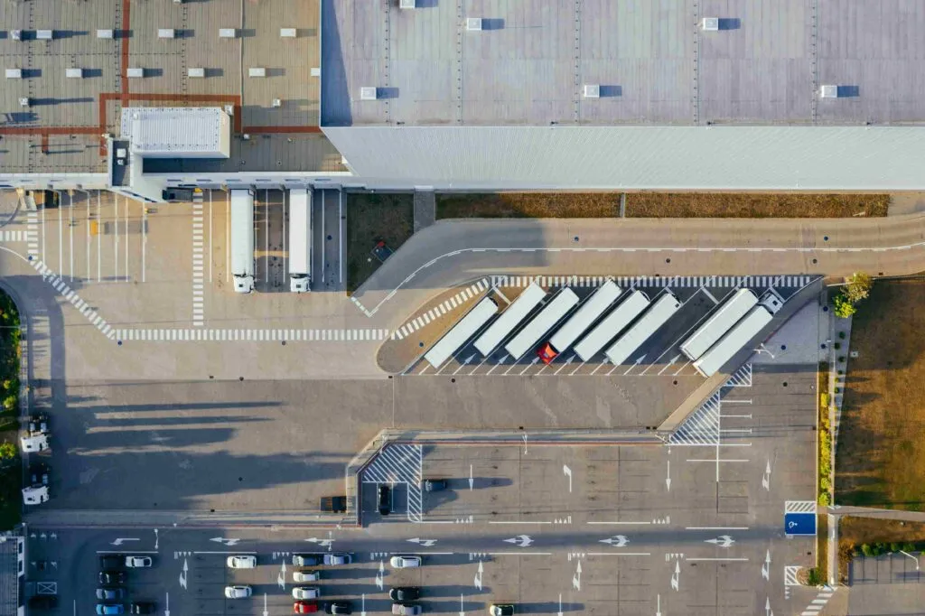 Top-down aerial drone view of a logistics distribution warehouse with semi-trucks parked at loading docks