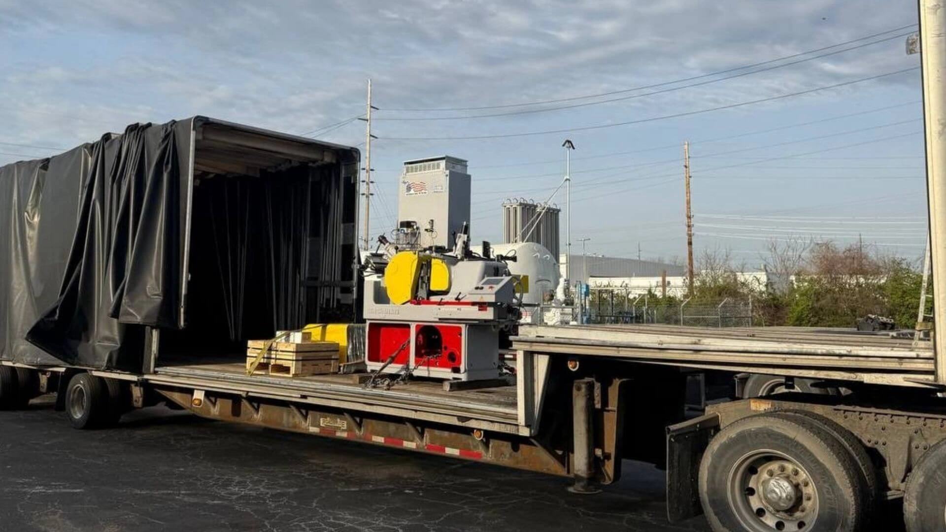 Curtain side Conestoga flatbed trailer carrying an industrial metal cutting saw machine and equipment on wooden pallets